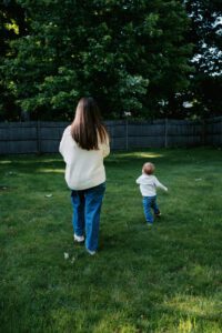 A mother and toddler wearing jeans and white sweaters dance and play in their backyard in Acton, Massachussets