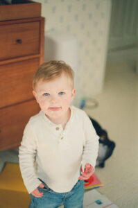 A blonde toddler in a white sweater with blue eyes in a blue and white nursery in Littleton, Massachusetts.