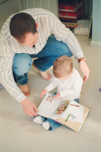 A father and son read a book in a blue and white nursery in Acton, Massachusetts.