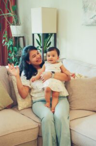 A mother holds her one year old daughter on her lap and waves on the couch in their apartment in Cambridge, Massachusetts. Captured on 35mm film.