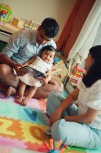 A father plays with his one year old daughter on a colorful play mat on the floor of their apartment in Cambridge, Massachusetts, while the mother looks on. Captured on 35mm film.