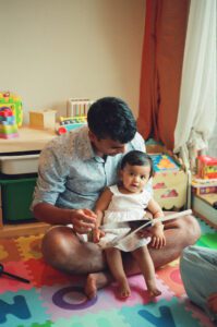 A father reads with his one year old daughter on a colorful play mat on the floor of their apartment in Cambridge, Massachusetts. Captured on 35mm film.