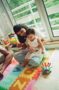 A mother reads to her one year old daughter on a colorful play mat on the floor of their apartment in Cambridge, Massachusetts. Captured on 35mm film.