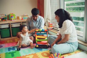 A mother and father play with their one year old daughter on a colorful play mat on the floor of their apartment in Cambridge, Massachusetts. Captured on 35mm film.