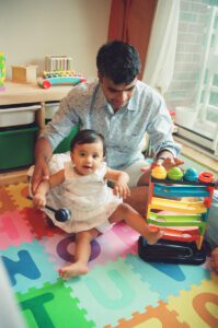 A father plays with his one year old daughter on a colorful play mat on the floor of their apartment in Cambridge, Massachusetts. Captured on 35mm film.
