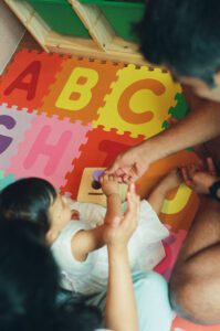 A closeup image of a mother and father's hands playing with their one year old daughter on a colorful play mat on the floor of their apartment in Cambridge, Massachusetts. Captured on 35mm film.