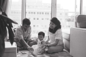A black and white image of mother and father playing with their one year old daughter on the floor of their apartment in Cambridge, Massachusetts. Captured on 35mm film.