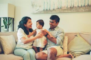 A mother and father hold their one year old daughter between them and smile at her on the couch in their apartment in Cambridge, Massachusetts. Captured on 35mm film.