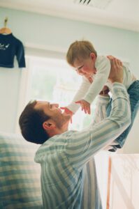 A father lifts his son in the air in a blue and white nursery in Acton, Massachusetts.