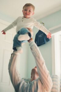A father lifts his son in the air in a blue and white nursery in Acton, Massachusetts.