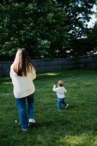 A mother and toddler wearing jeans and white sweaters dance and play in their backyard in Acton, Massachussets